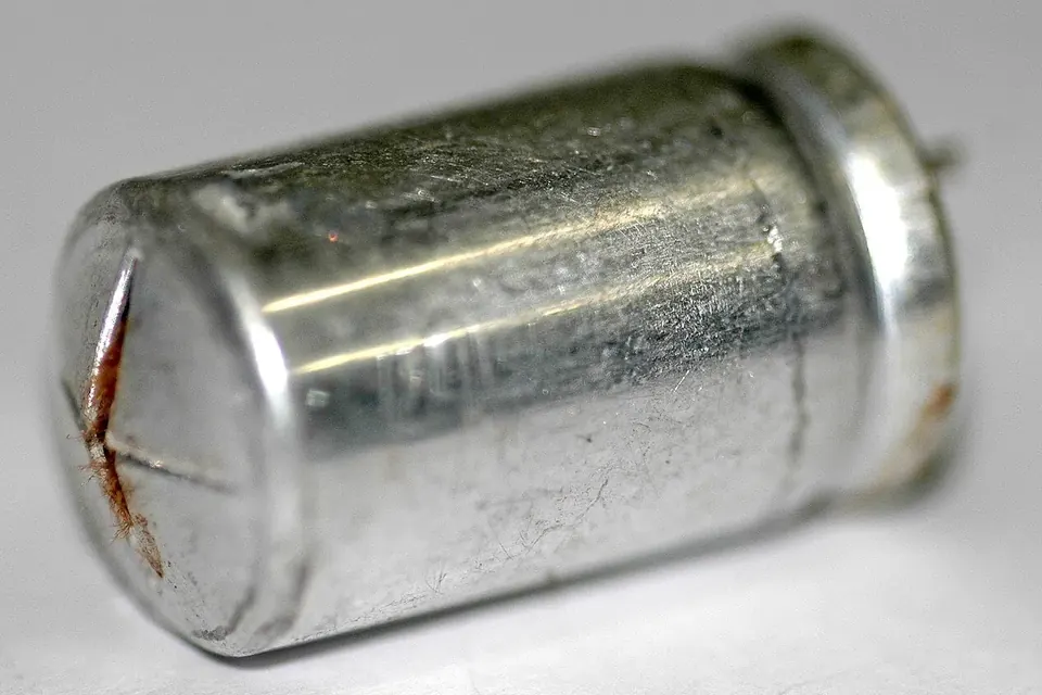 Close-up of a failed metal-can electrolytic capacitor with its end split open and stained by leaked electrolyte
