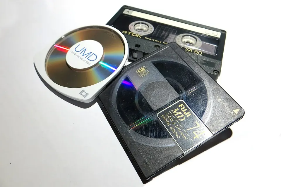 A MiniDisc, a Universal Media Disc and a Compact Cassette laid side by side to compare their sizes