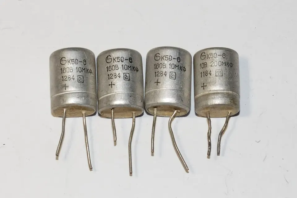 Four old metal-can electrolytic capacitors with Cyrillic markings, standing on their wire leads