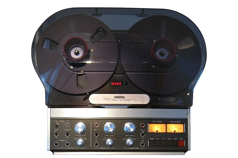 An open-reel tape recorder with a smoked dust cover over its reels, and level controls and VU meters below
