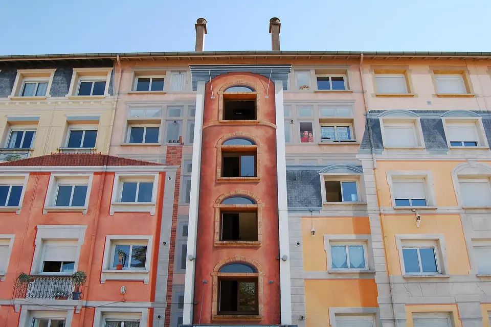 The painted facade of an old apartment building with rows of shuttered windows, small balconies and a tall arched stairwell window