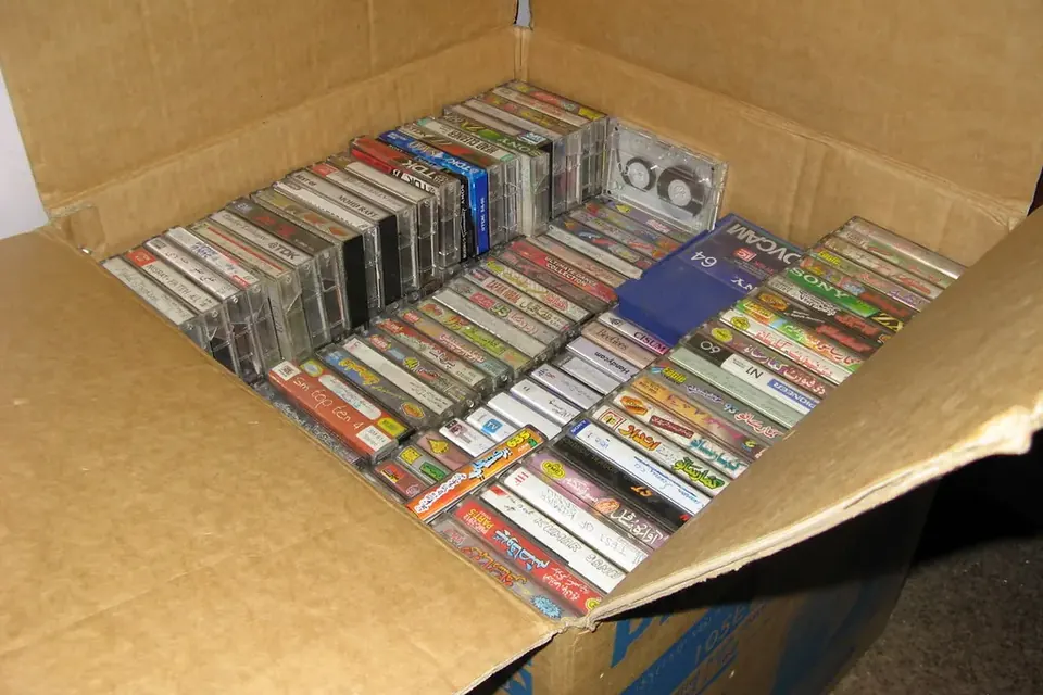 A cardboard box full of recorded audio cassettes in their cases, seen from above