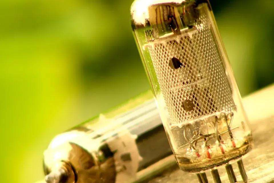 Close-up of a glass vacuum tube with its metal plate structure visible inside, lying beside another tube on a wooden surface